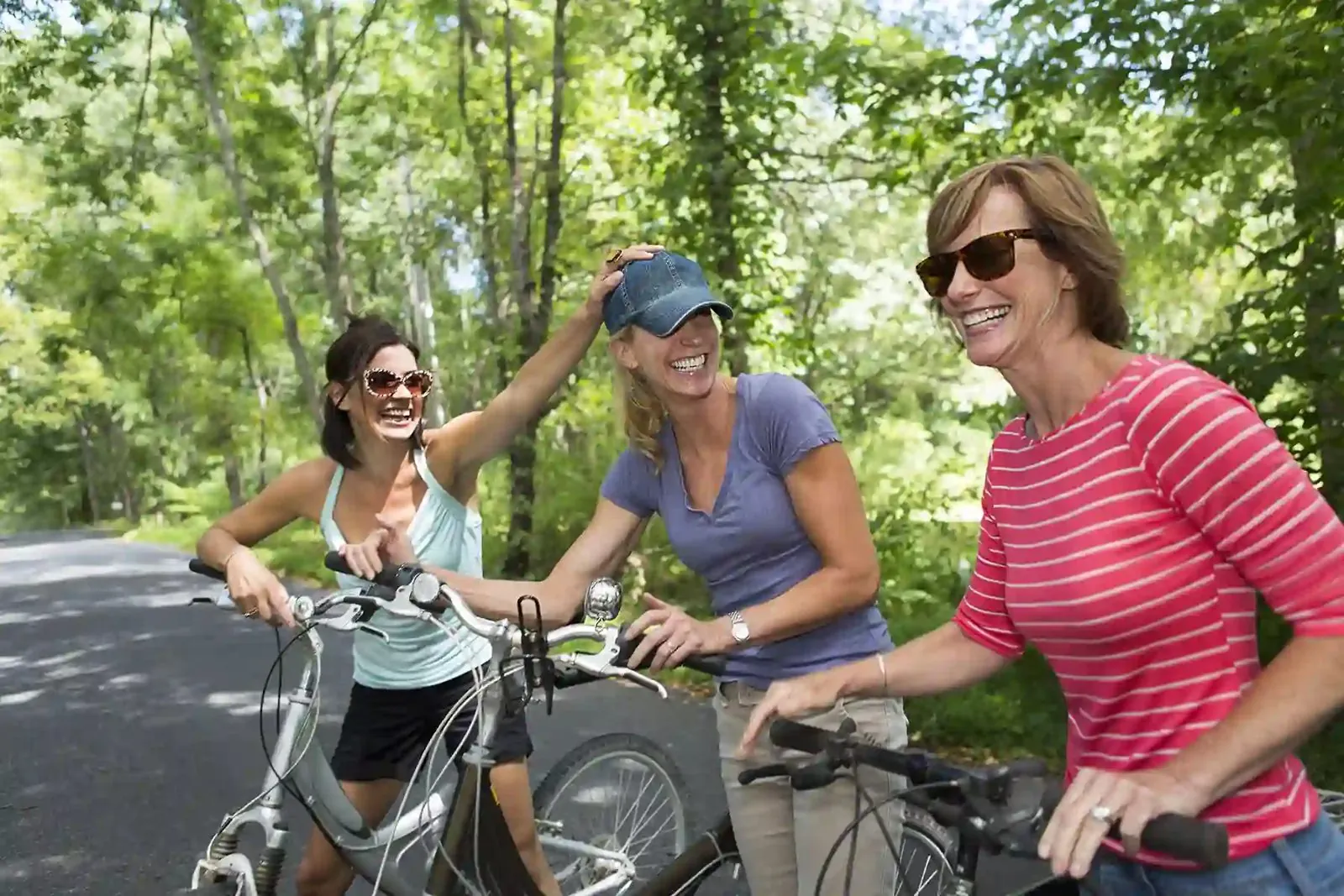 Three women riding bicycles on a tree-lined trail
